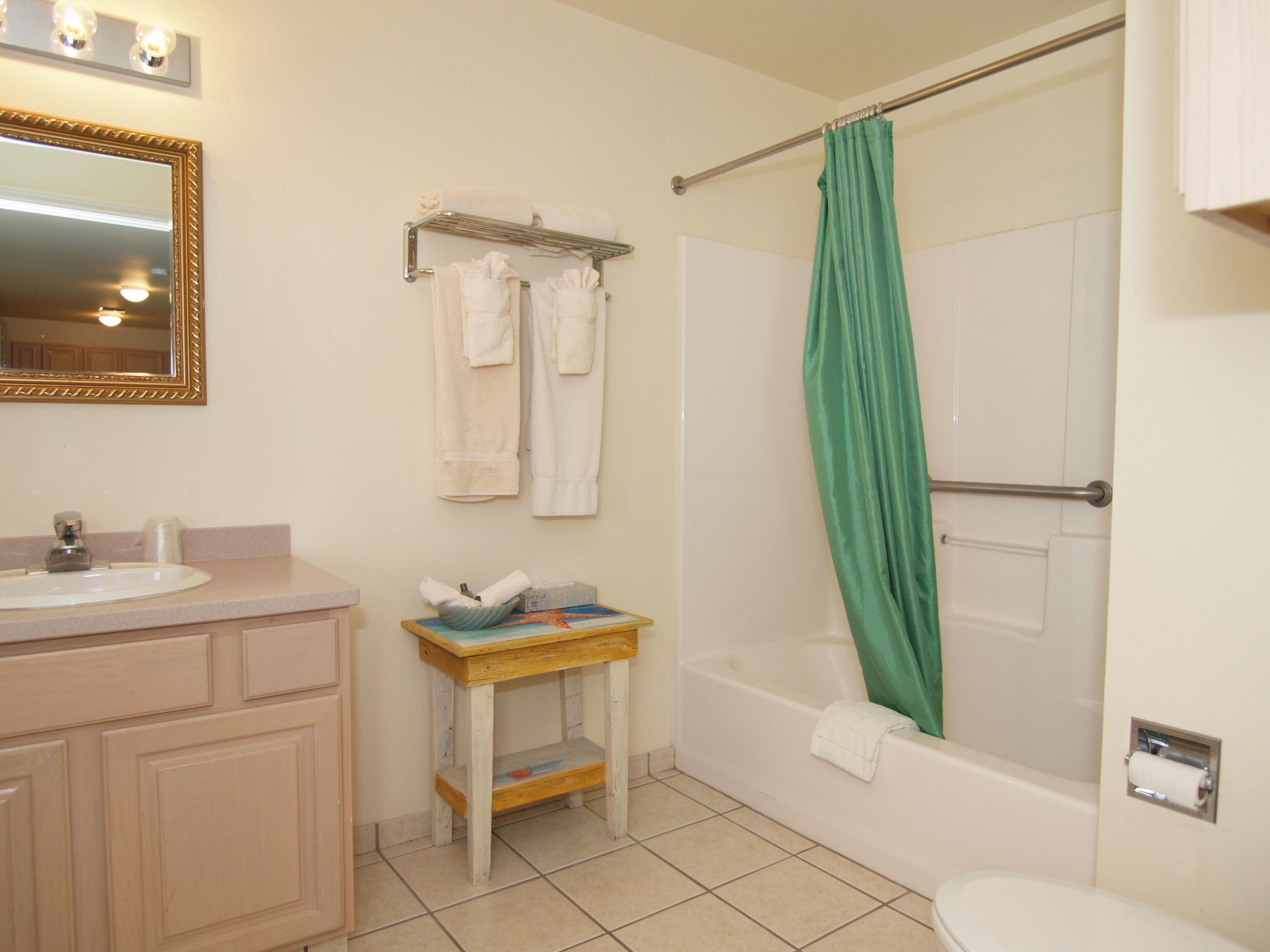 Un baño con lavamanos, espejo, toallero, cortina de ducha y retrete.