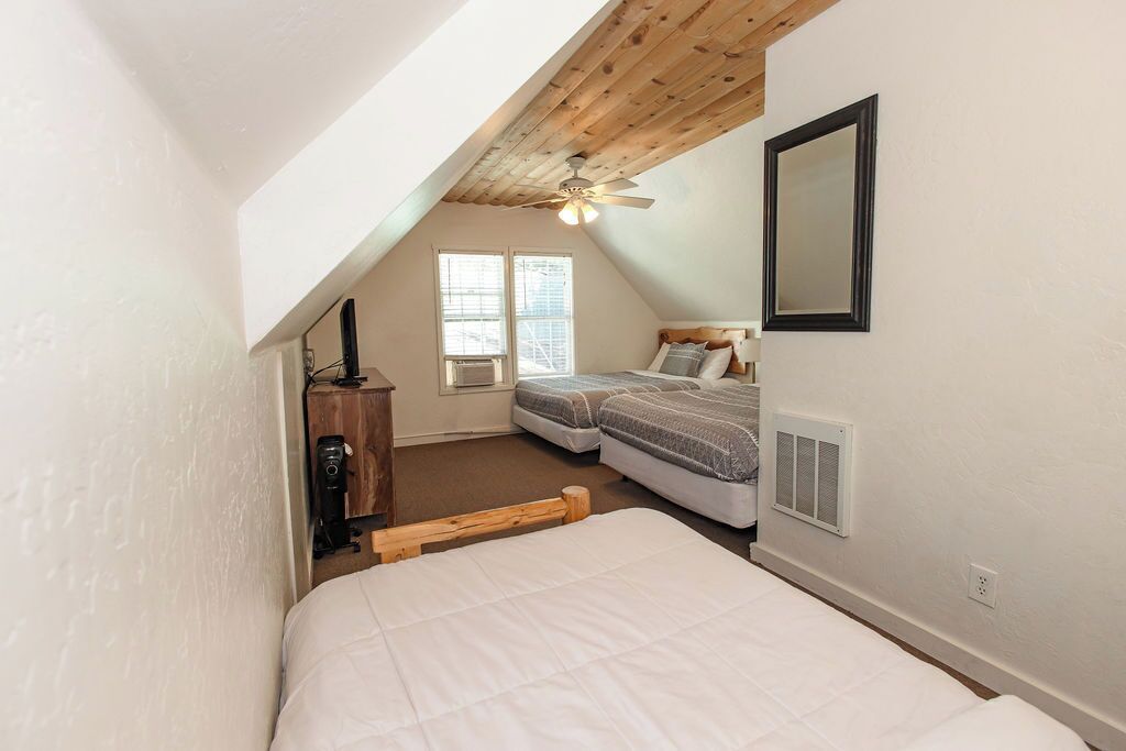 A bedroom with a sloped ceiling, two beds, a ceiling fan, and a window.