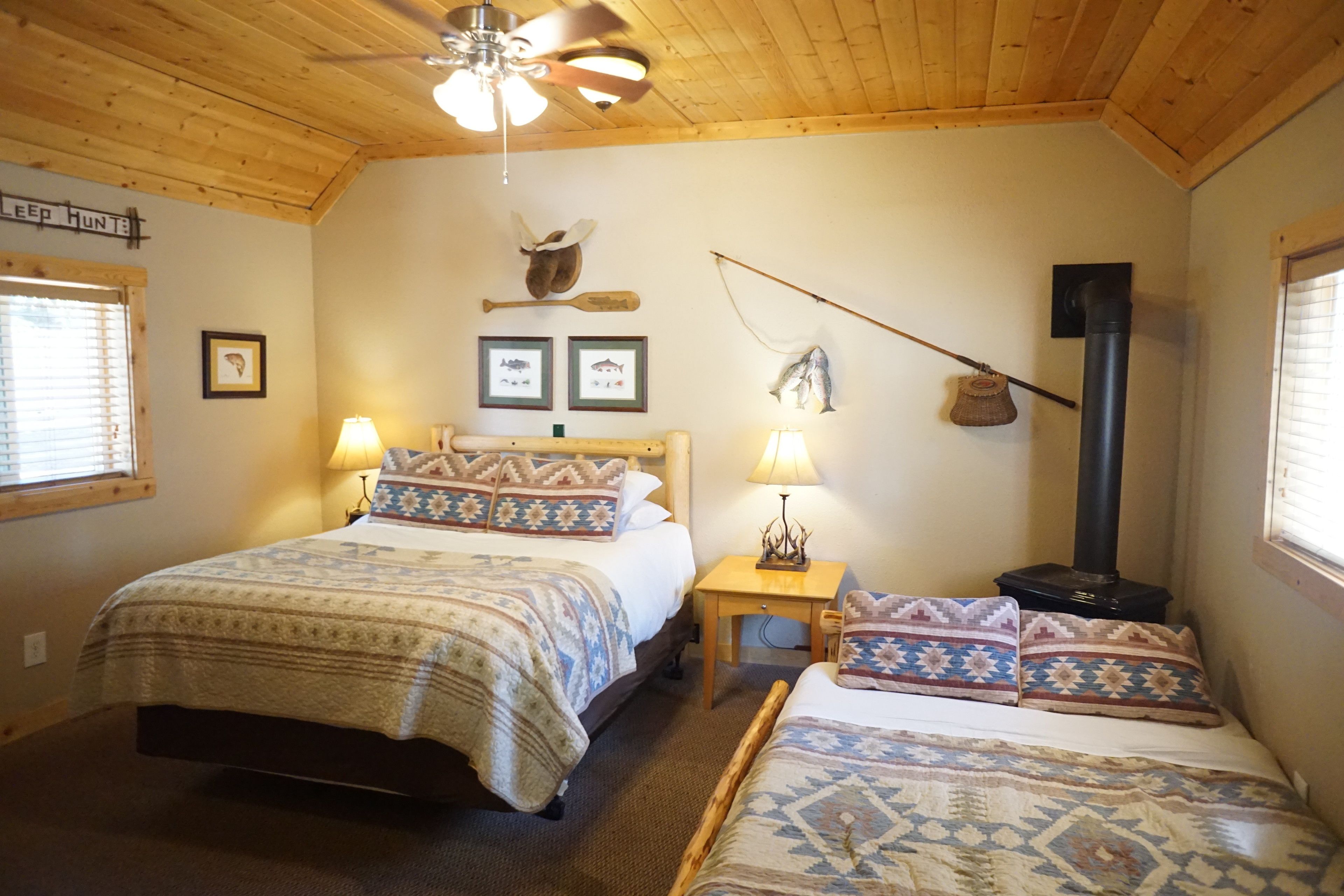 A cozy bedroom with two beds, a ceiling fan, a fireplace, and framed pictures on the wall.