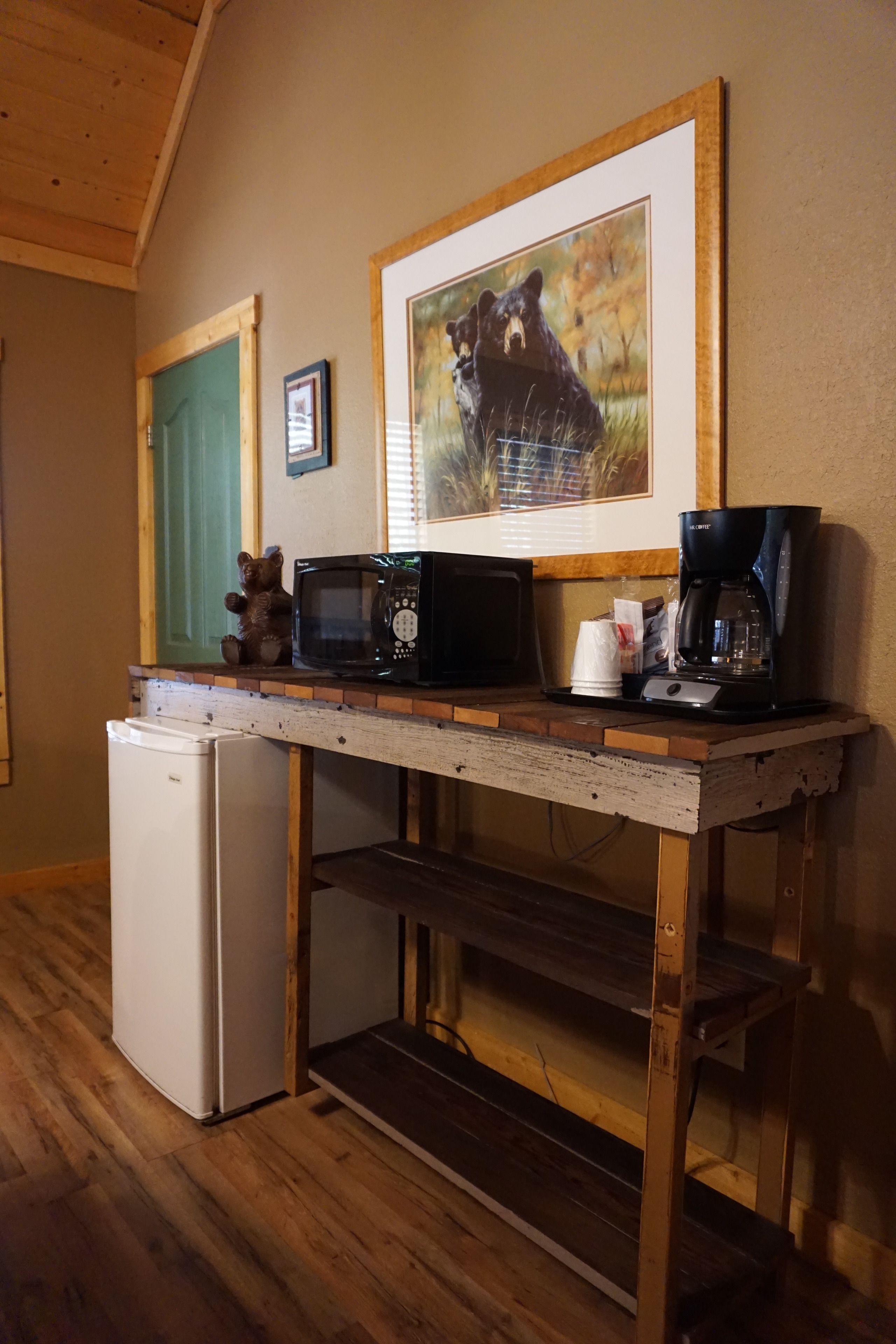 Una cocina equipada con refrigerador, microondas, cafetera y un cuadro de un oso en la pared.