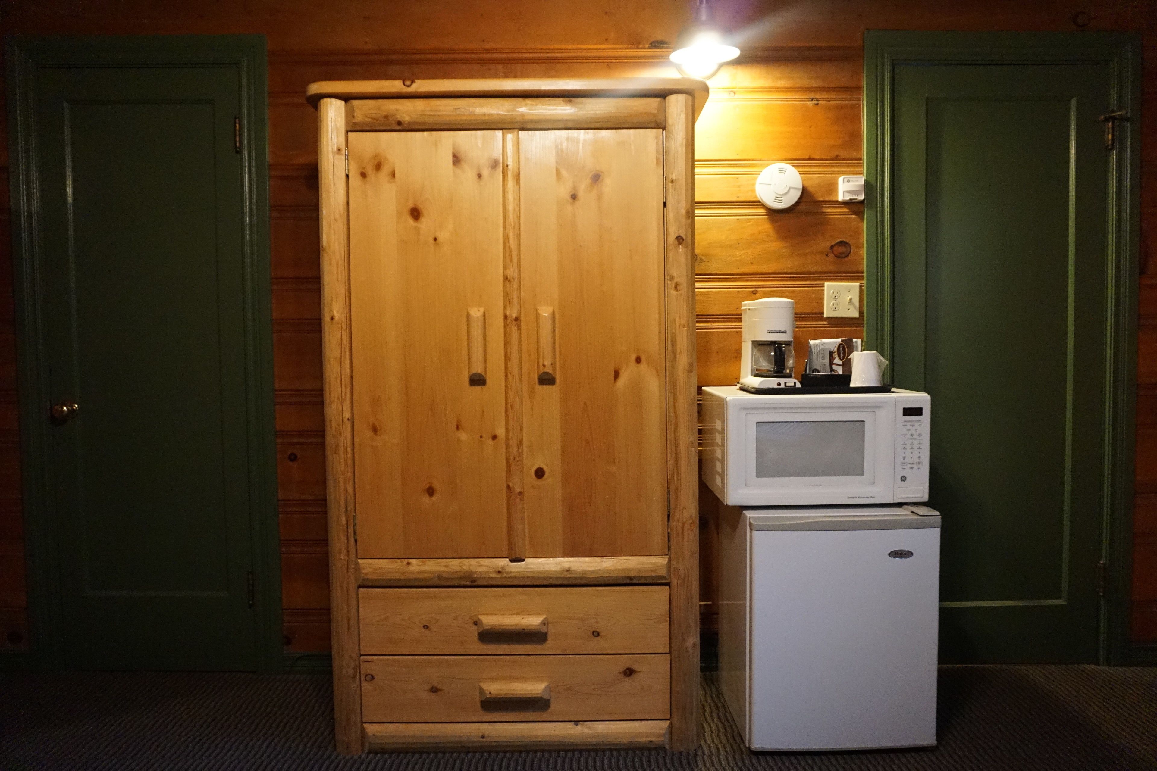 A wooden wardrobe with two doors and a small refrigerator with a microwave on top.