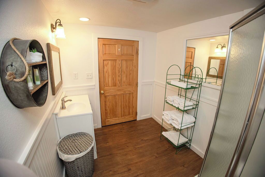 Un baño con puerta de madera, lavamanos blanco, perchero y espejo.