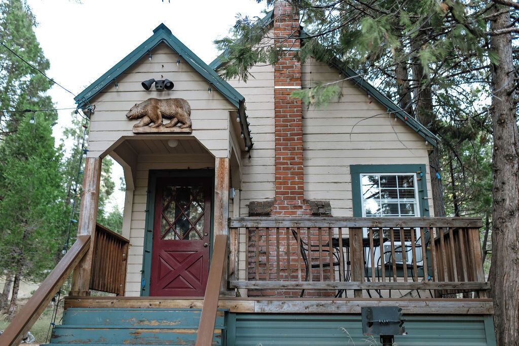 Une cabane rustique avec une véranda en bois, une porte rouge et une sculpture d’ours à l’avant.