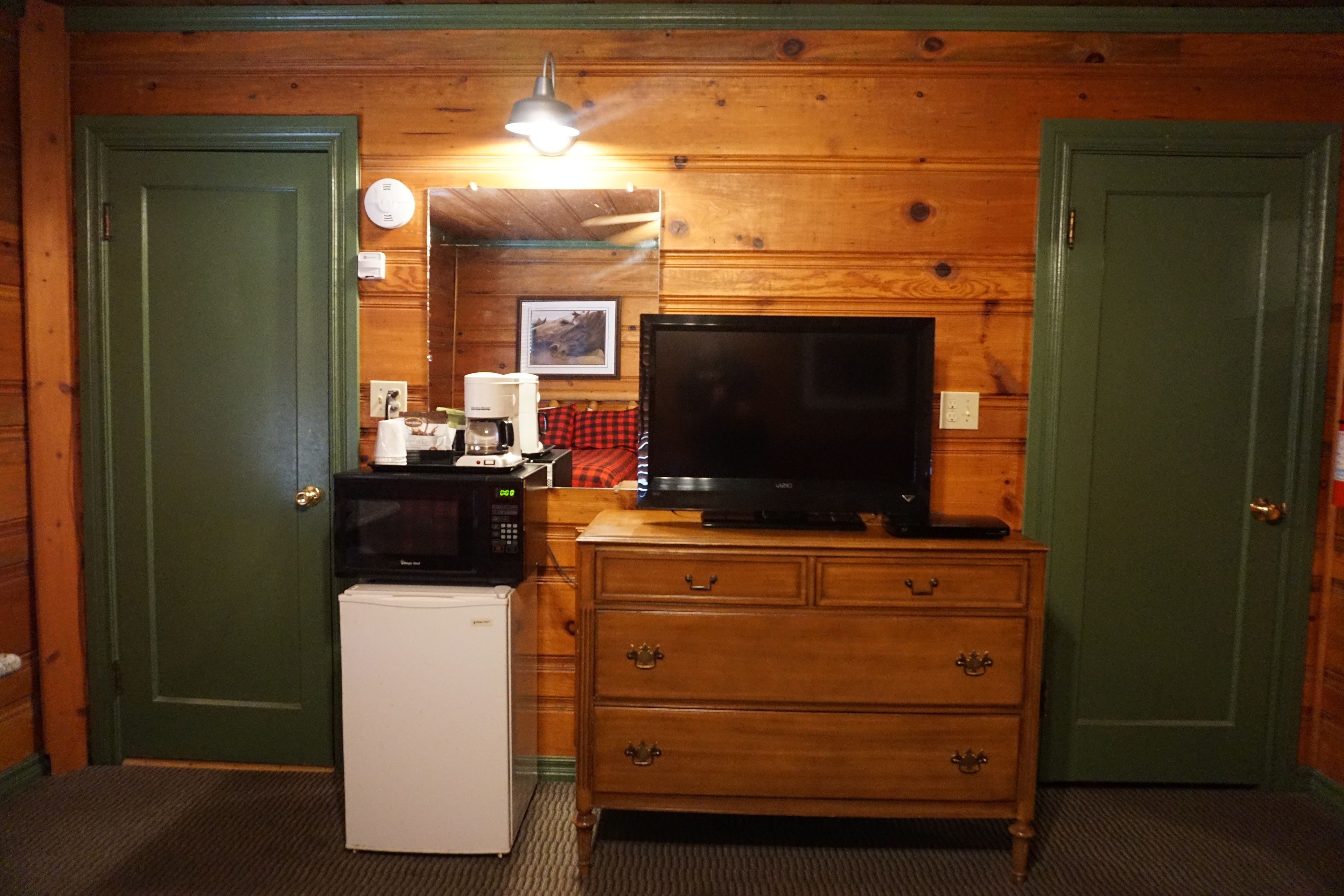 Una habitación con paredes de madera, un televisor sobre una cómoda de madera, un microondas y un refrigerador.