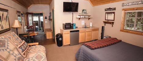 A cozy cabin interior with a sofa, a bed, a kitchenette, and a television.