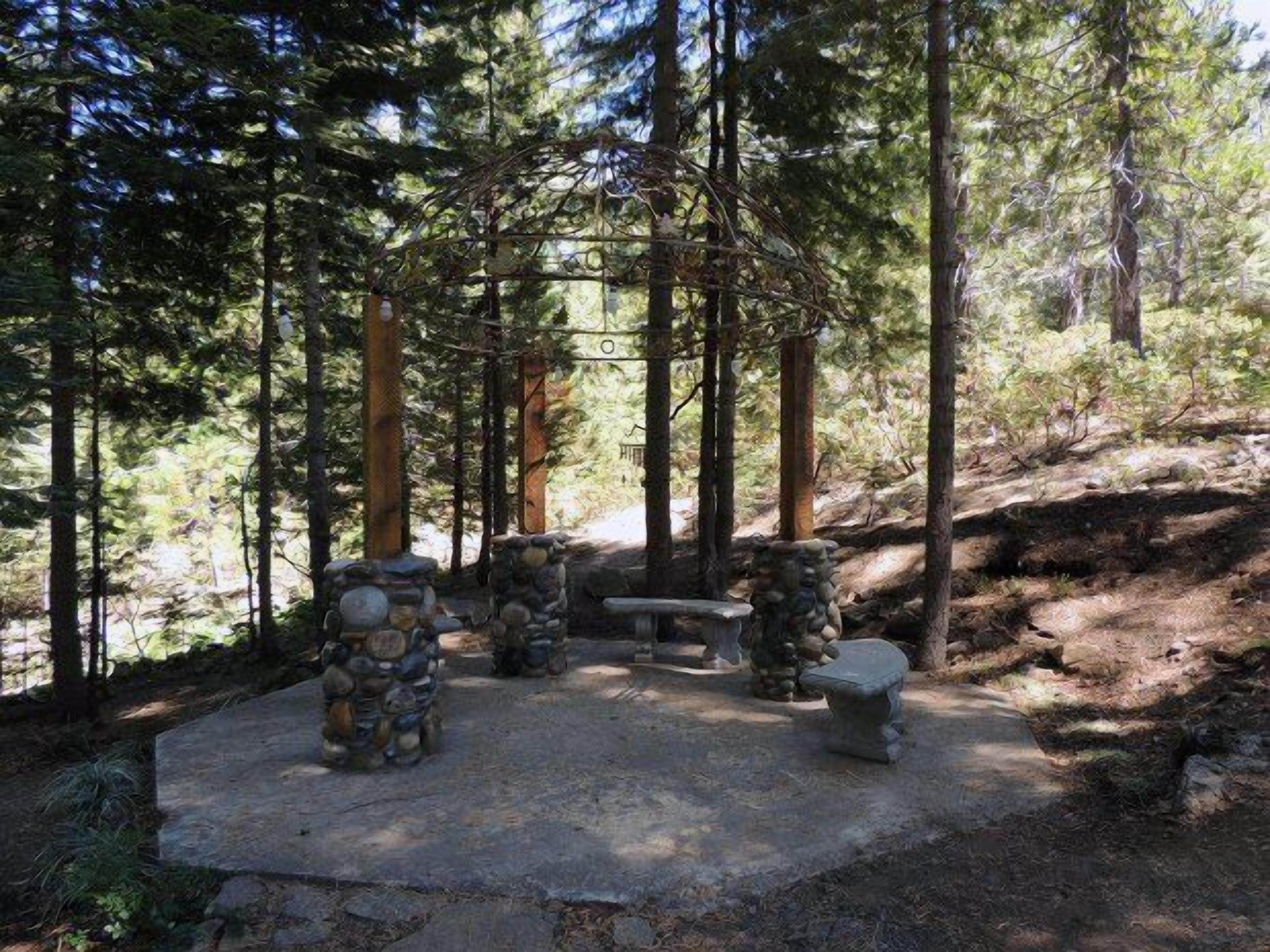 Un espace extérieur aménagé avec des sièges en pierre, entouré de grands arbres dans un cadre forestier.