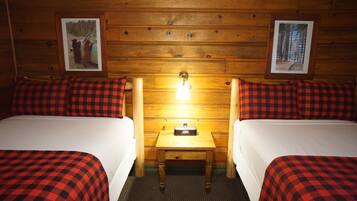 Habitación con dos camas, cada una con ropa de cama a cuadros rojo y negro, una mesita de noche de madera con lámpara, y paredes de madera decoradas con cuadros.