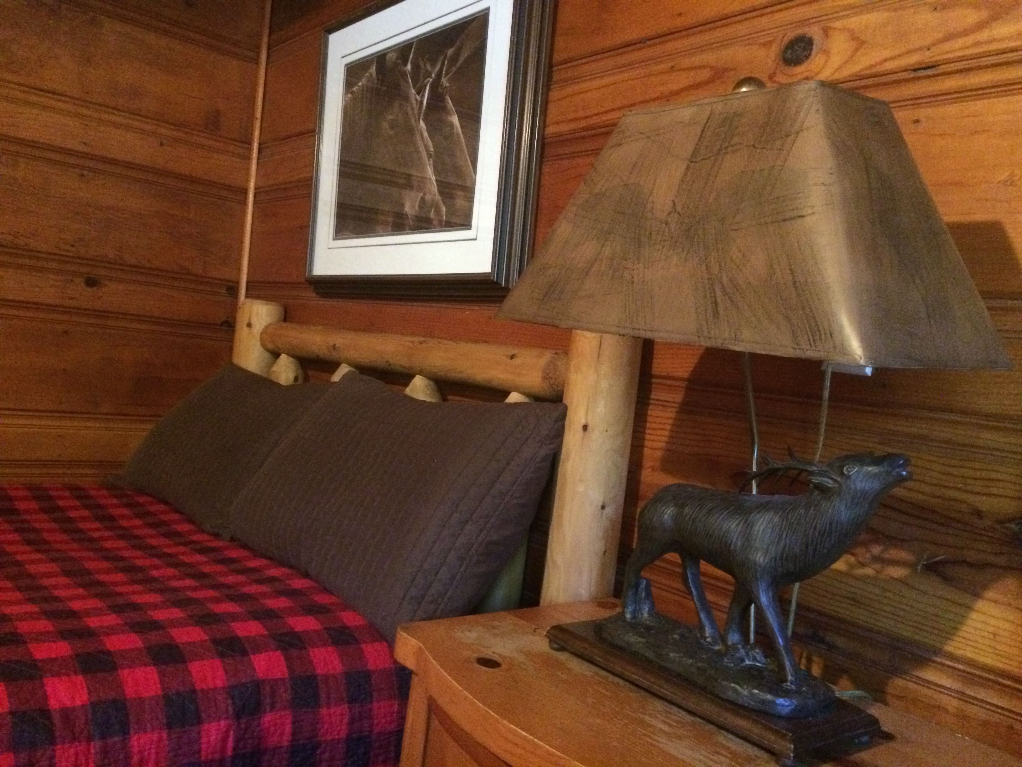 Una habitación de cabaña de madera con una cama, una lámpara y un cuadro en la pared.