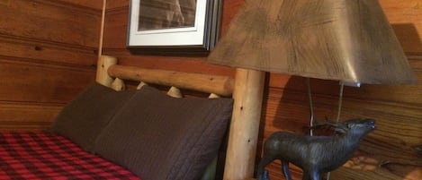 Una habitación de cabaña de madera con una cama, una lámpara y un cuadro en la pared.