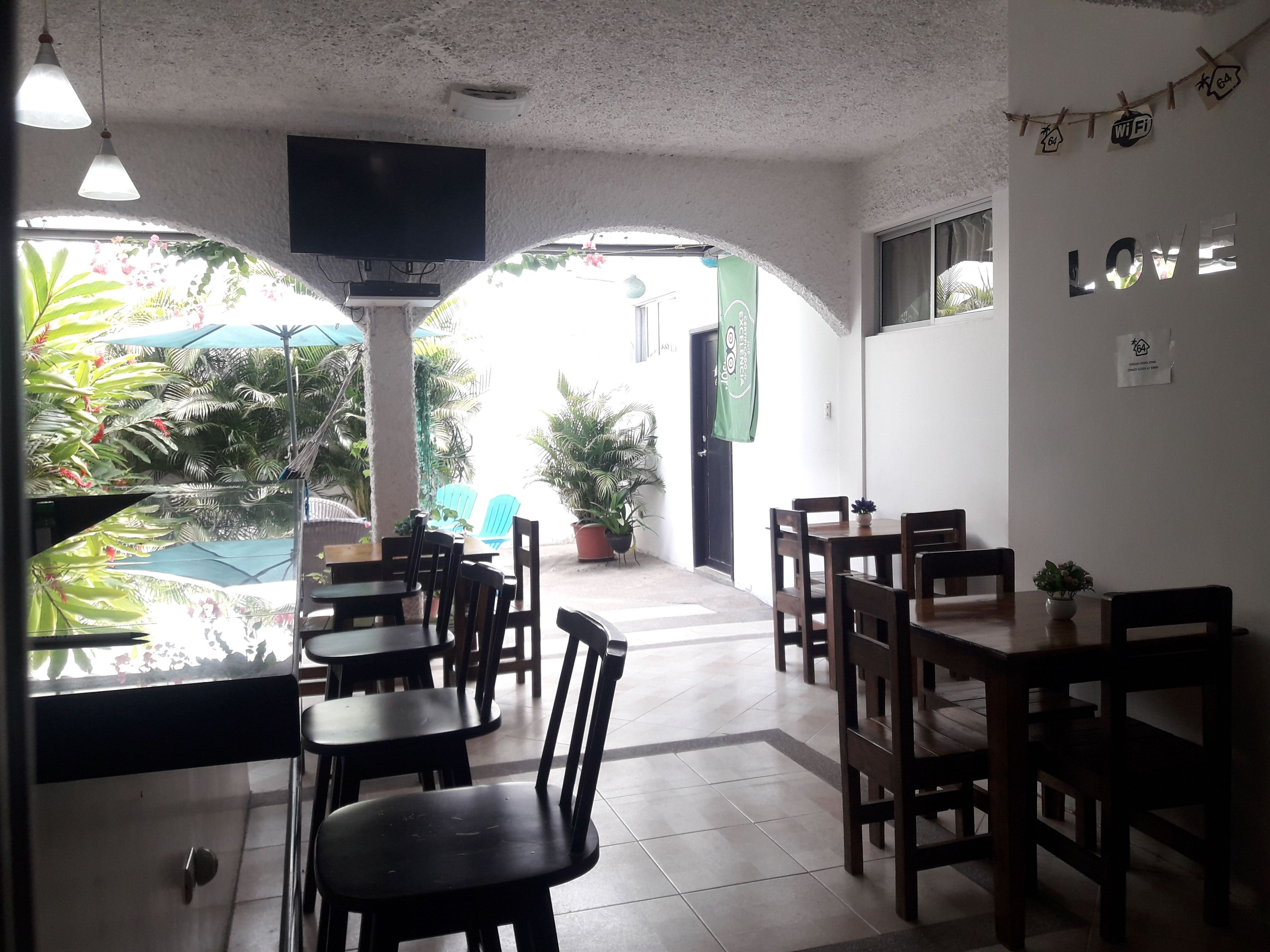 A restaurant with wooden tables and chairs, a TV mounted on the wall, and a view of the outdoors with plants and umbrellas.