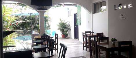 A restaurant with wooden tables and chairs, a TV mounted on the wall, and a view of the outdoors with plants and umbrellas.