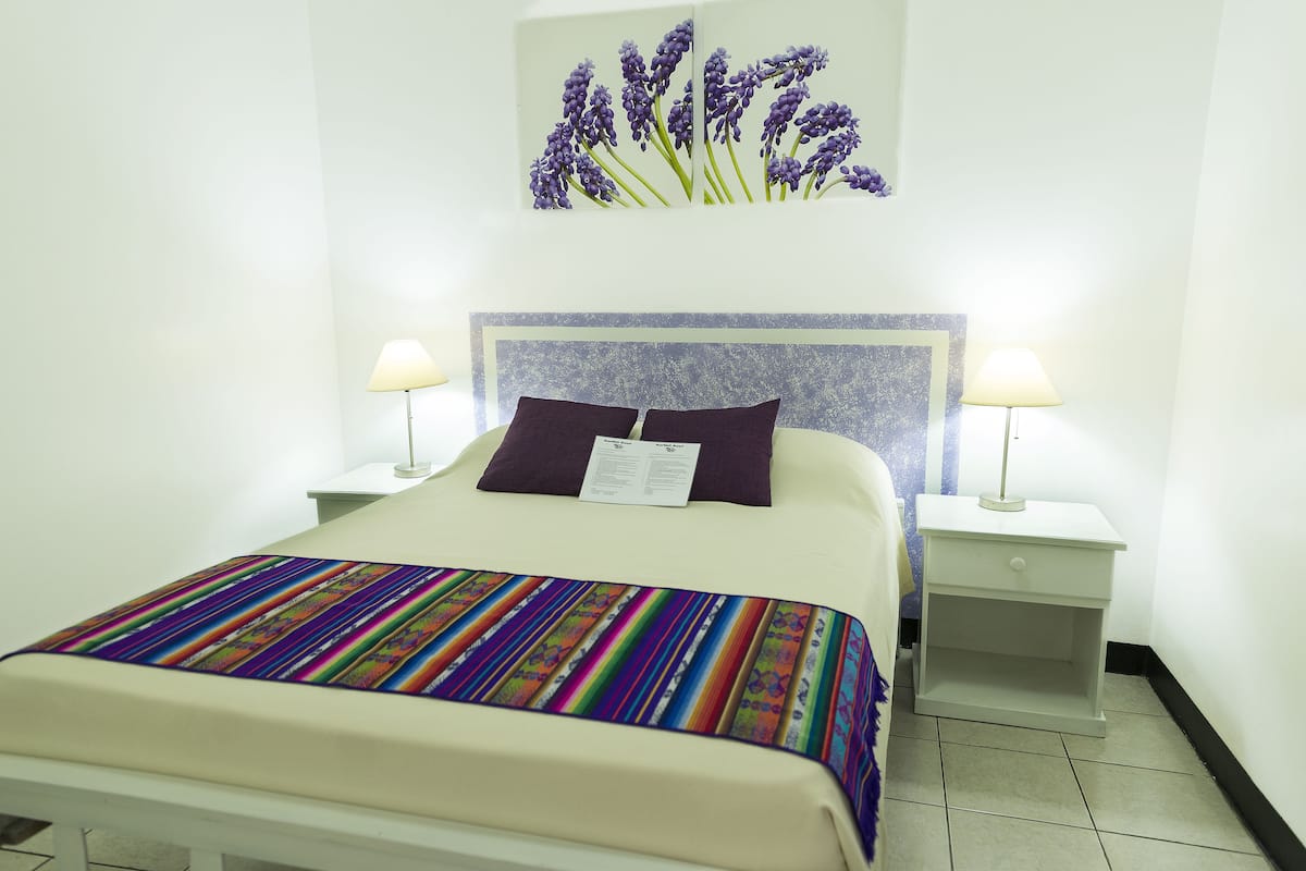 A neatly made bed with a colorful blanket, two bedside lamps, and a headboard with a floral design.