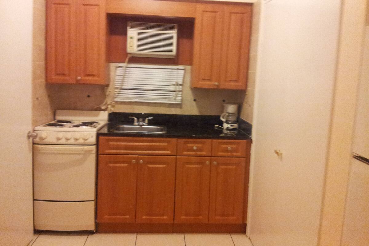A small kitchen with wooden cabinets, a stove, a sink, and a coffee maker.