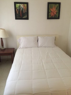 Un letto con biancheria bianca, un comodino con una lampada e due quadri appesi al muro.