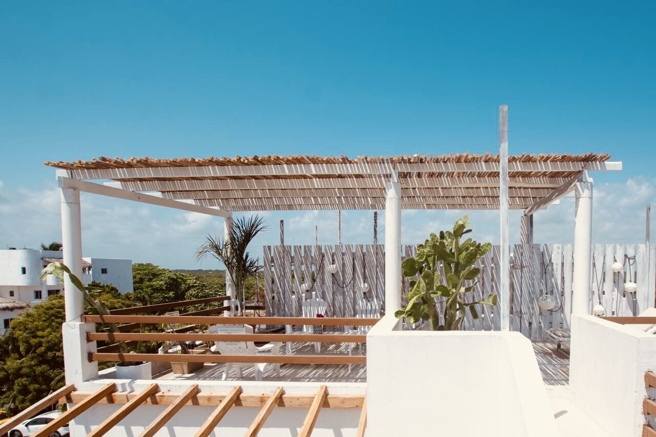 A rooftop terrace with a wooden pergola, white railings, and potted plants.
