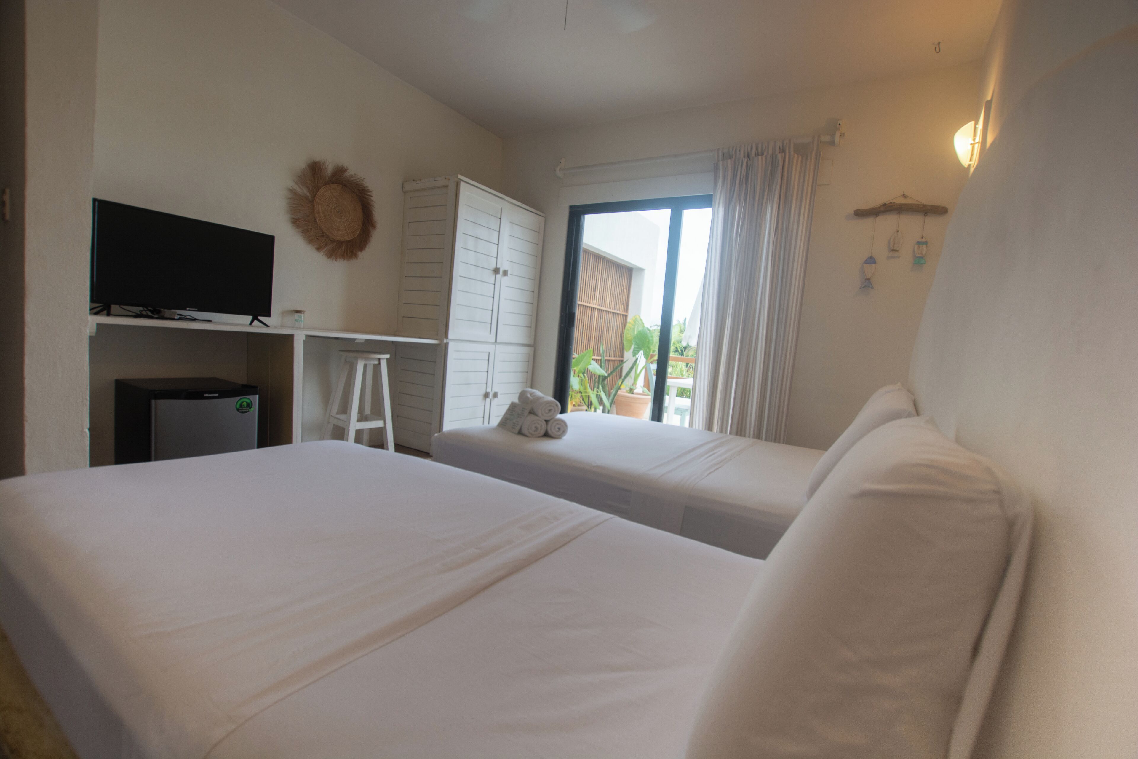A hotel room with two beds, a TV, a desk, and a window with curtains.