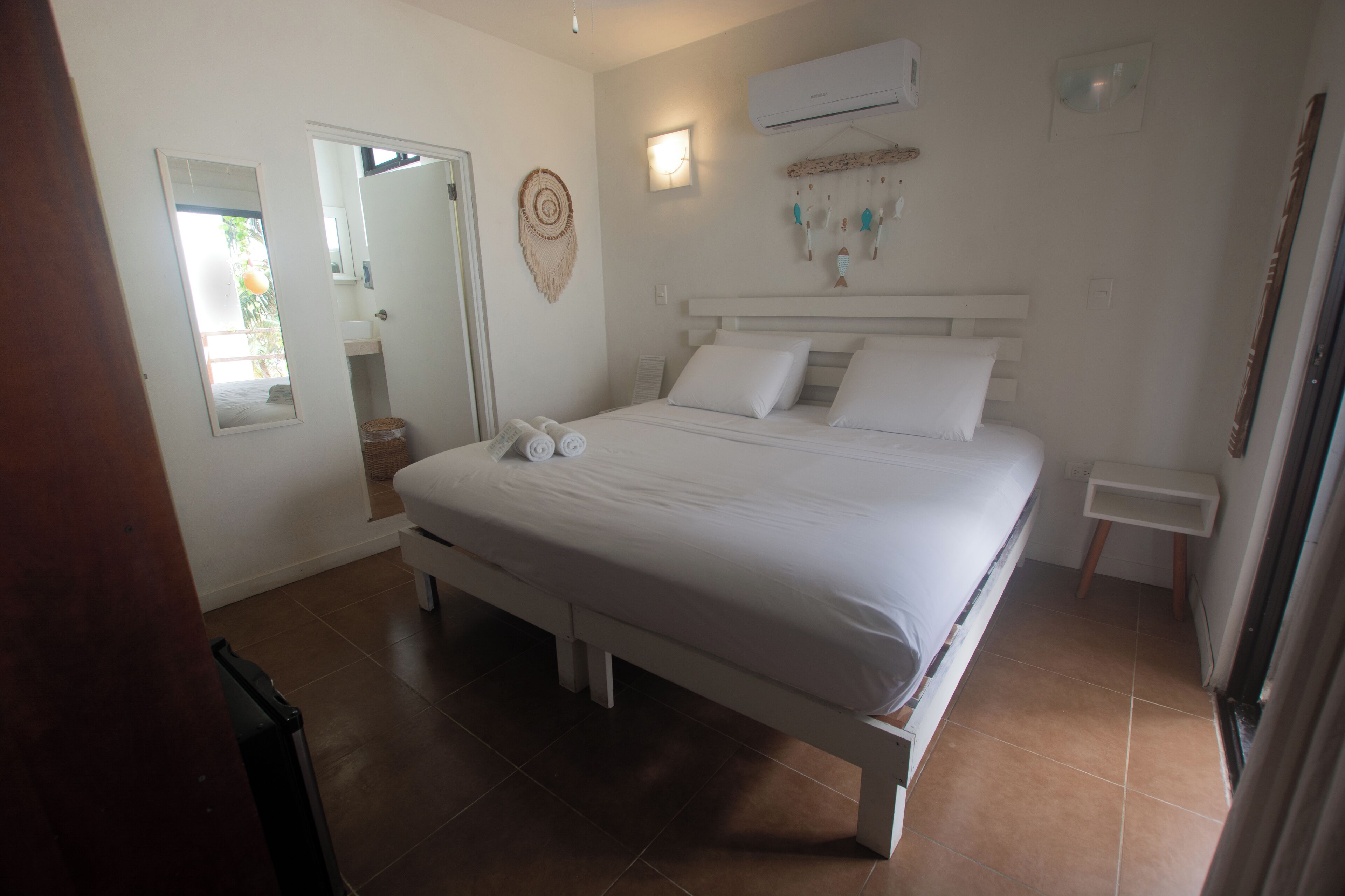 Une chambre à coucher comprenant un lit, une table de chevet, un miroir et un appareil de climatisation fixé au mur.