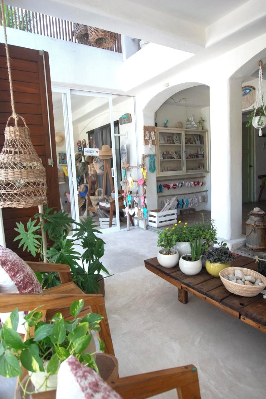 Un espacio interior con una mesa de madera, plantas en macetas y estantes con diversos objetos.