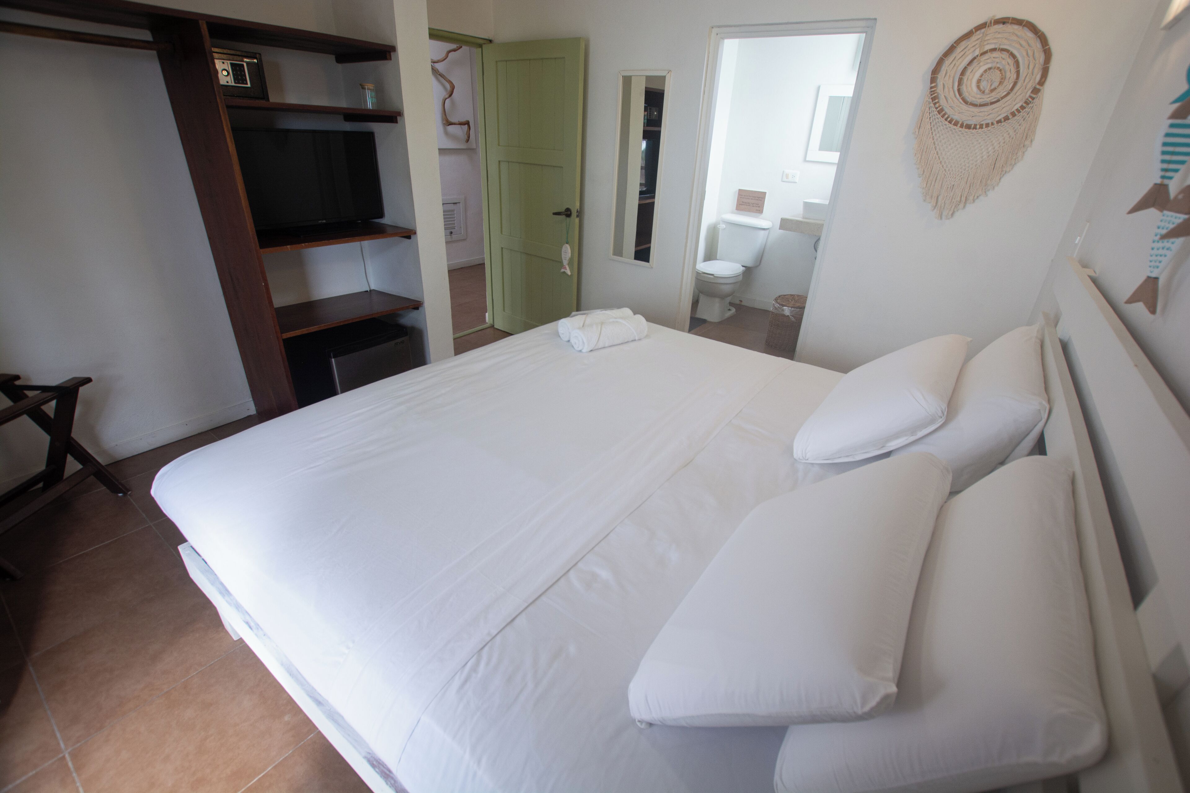 Une chambre avec un grand lit, un téléviseur posé sur une étagère, une armoire et une salle de bain visible à travers une porte ouverte.