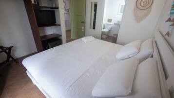 Une chambre avec un grand lit, un téléviseur posé sur une étagère, une armoire et une salle de bain visible à travers une porte ouverte.