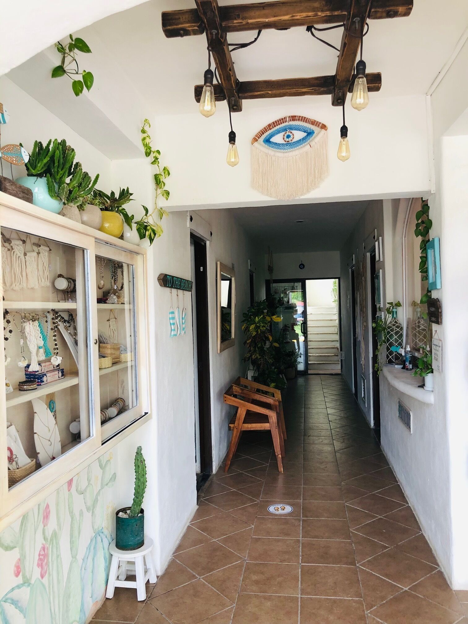 A hallway with a wooden ceiling, hanging light bulbs, and potted plants.