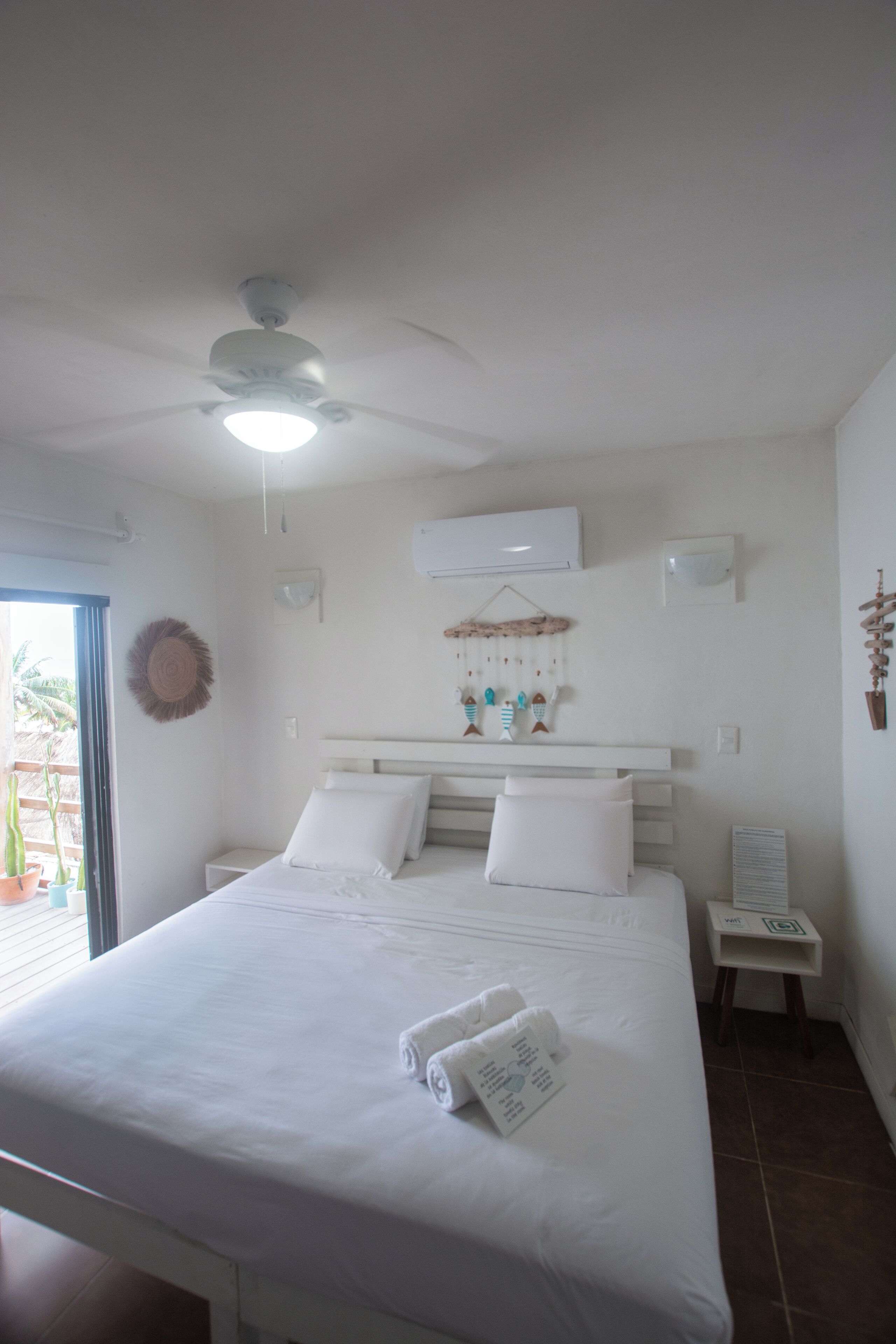 Quarto com cama, ventoinha no teto, ar condicionado, luminária na parede e uma mesinha de cabeceira.