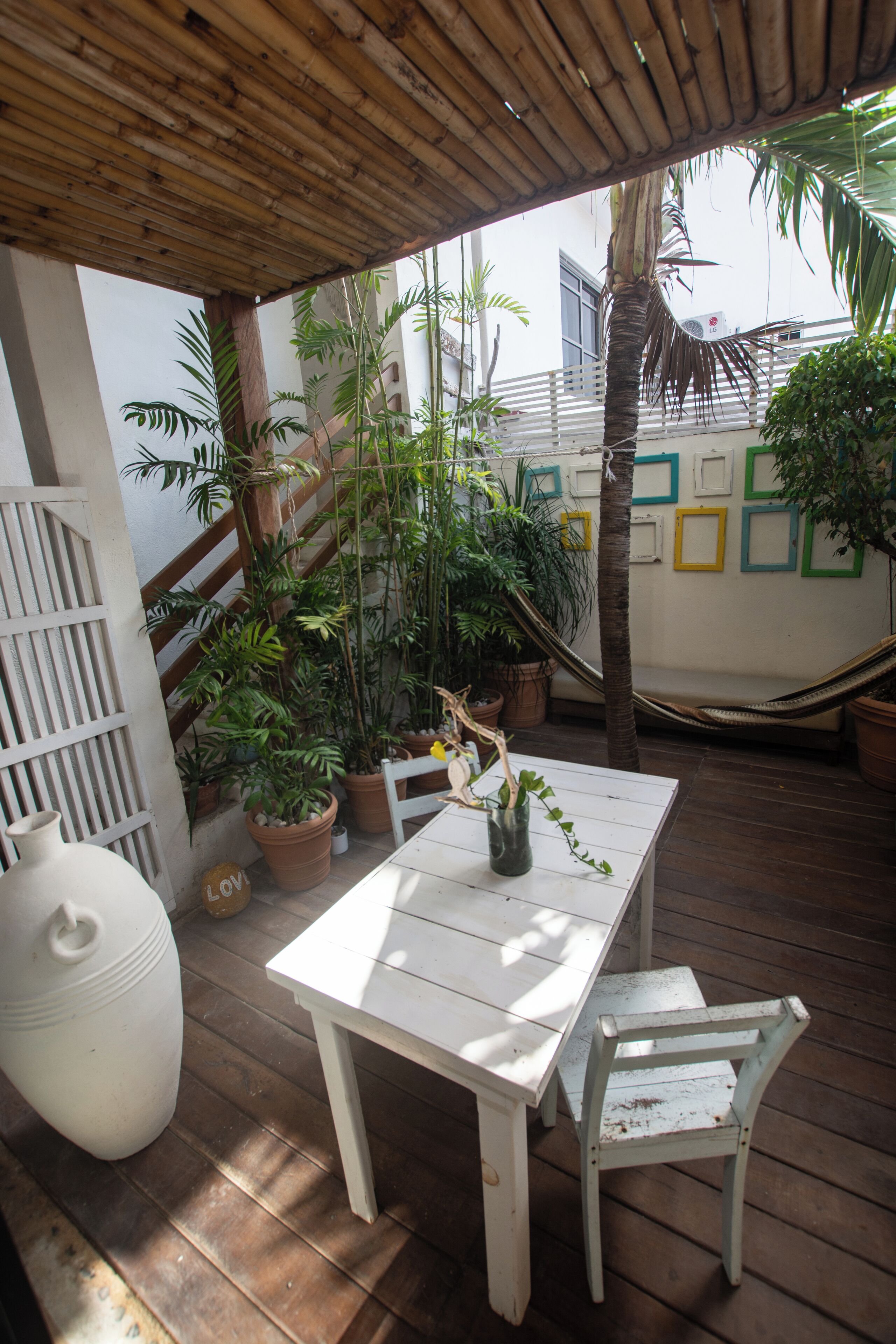 Een houten terras met een witte tafel en stoel, omringd door potplanten en een hangmat.