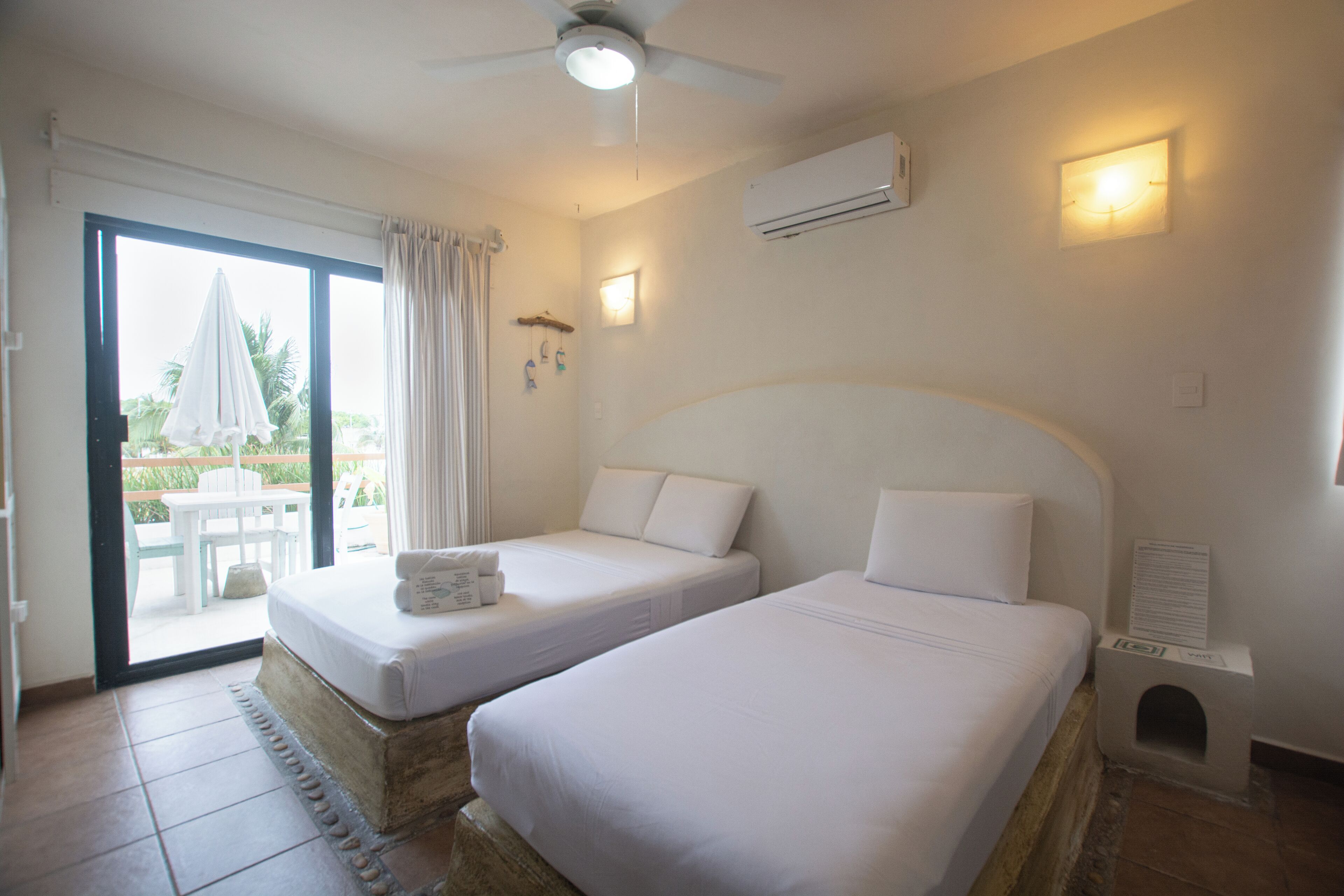 Een hotelkamer met twee bedden, een plafondventilator, een airconditioning en uitzicht op het omliggende landschap.