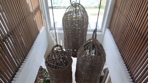 Vista desde una ventana con cestas de mimbre colgando, una planta en maceta y un atisbo de vegetación al exterior.