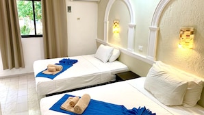 Habitación de hotel con dos camas, toallas color beige, cubrecamas azules y un espejo grande con apliques en la pared.