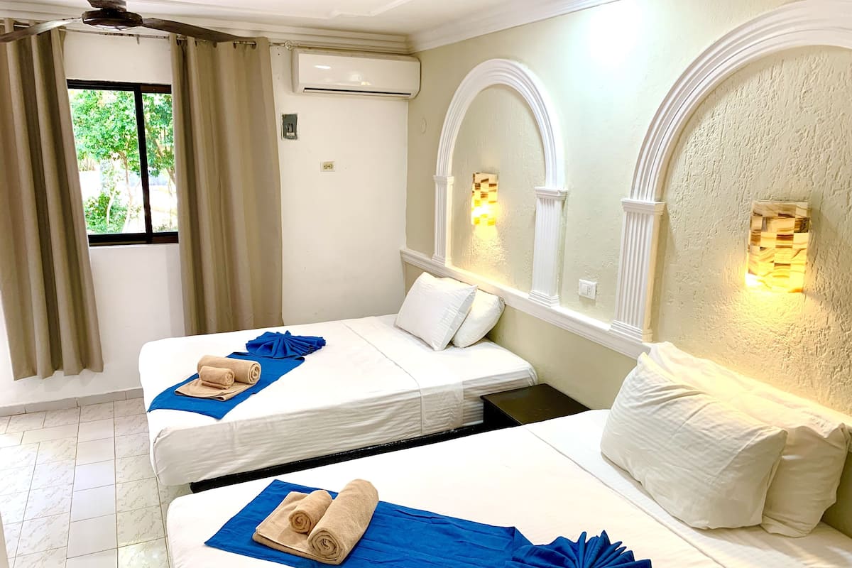 A hotel room with two beds, beige towels, blue bedspreads, and a large mirror with wall sconces.