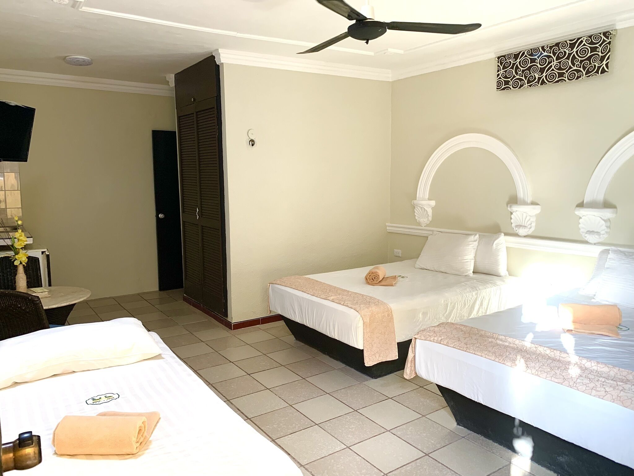 Habitació d'hotel amb dos llits, un ventilador de sostre, escriptori amb cadira i una taula petita amb un ram de flors.
