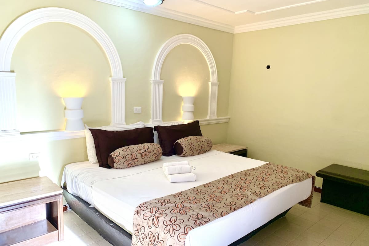 A neatly made bed with a floral bedspread, two pillows, and a bedside lamp.