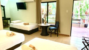 Habitación de hotel con dos camas, una mesita, una silla y un balcón con vistas a zonas verdes.