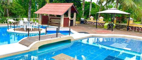 Una piscina con piso de baldosas, un pequeño pabellón y palmeras circundantes.