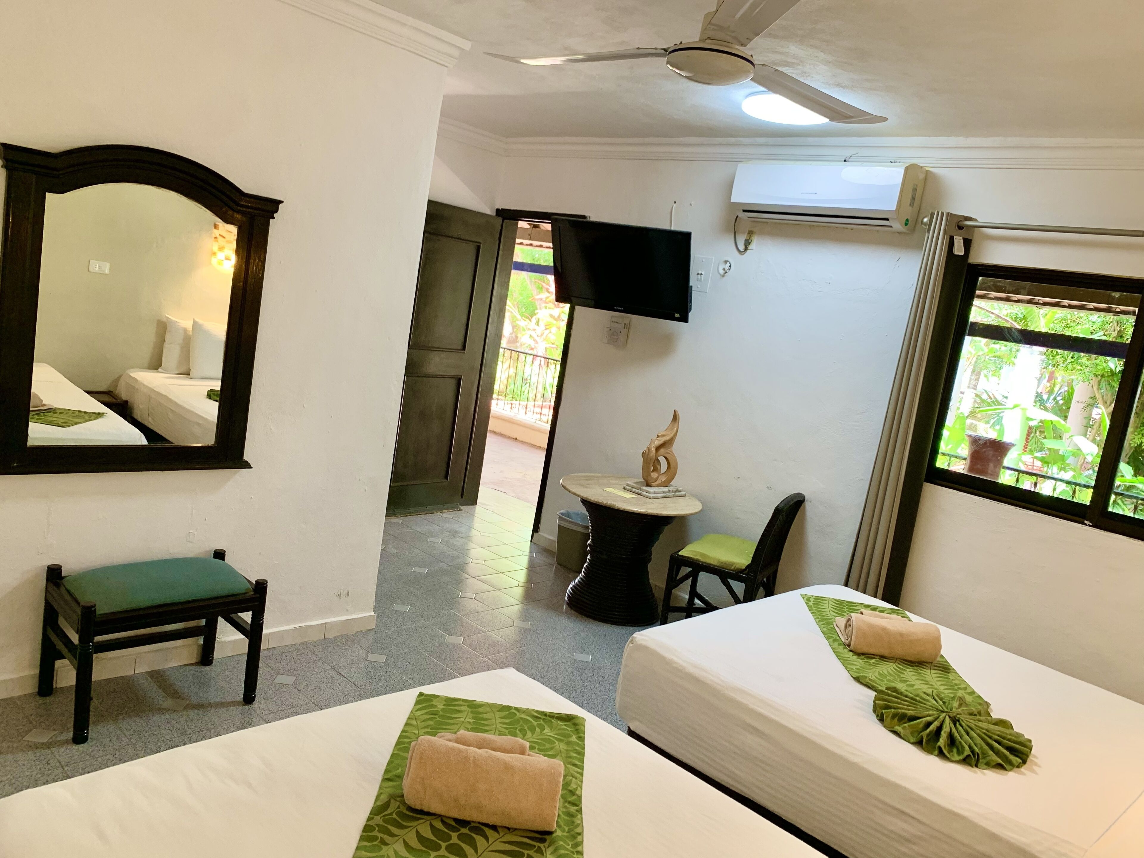 Habitación de hotel con dos camas, una mesita con un adorno, una silla, un televisor y una ventana con vista a zonas verdes.