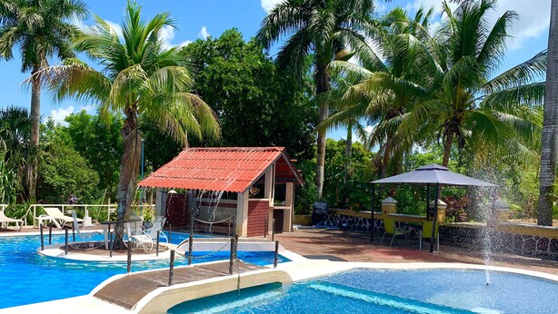 Piscina con una estructura de techo rojo, rodeada de palmeras y sillas de descanso.
