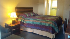 A hotel room with a bed, a bedside table with a lamp, a chair, and a desk with a telephone. - Holiday Lodge (Port Angeles)