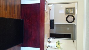 A room with a wooden floor, a dark brown desk, a black chair, a clock on the wall, and a framed picture. - Holiday Lodge (Port Angeles)