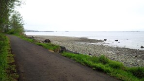 A paved path beside a rocky shoreline with a body of water and distant land in the background. - Holiday Lodge (Port Angeles)