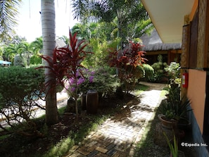 A paved pathway leading to a building with a thatched roof, surrounded by various plants and trees. - Veraneante Resort (Panglao)