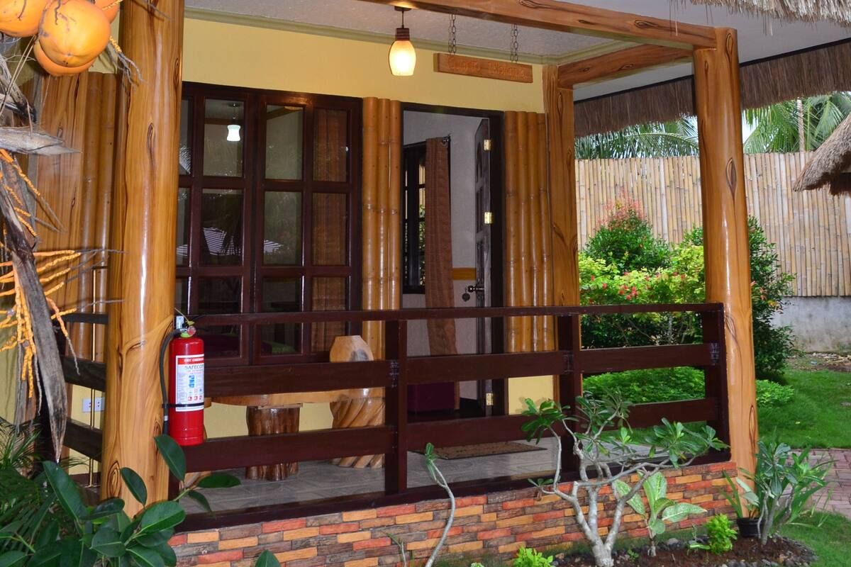 Estructura de madera con techo de paja, extintor y pequeño jardín con plantas y un sendero.