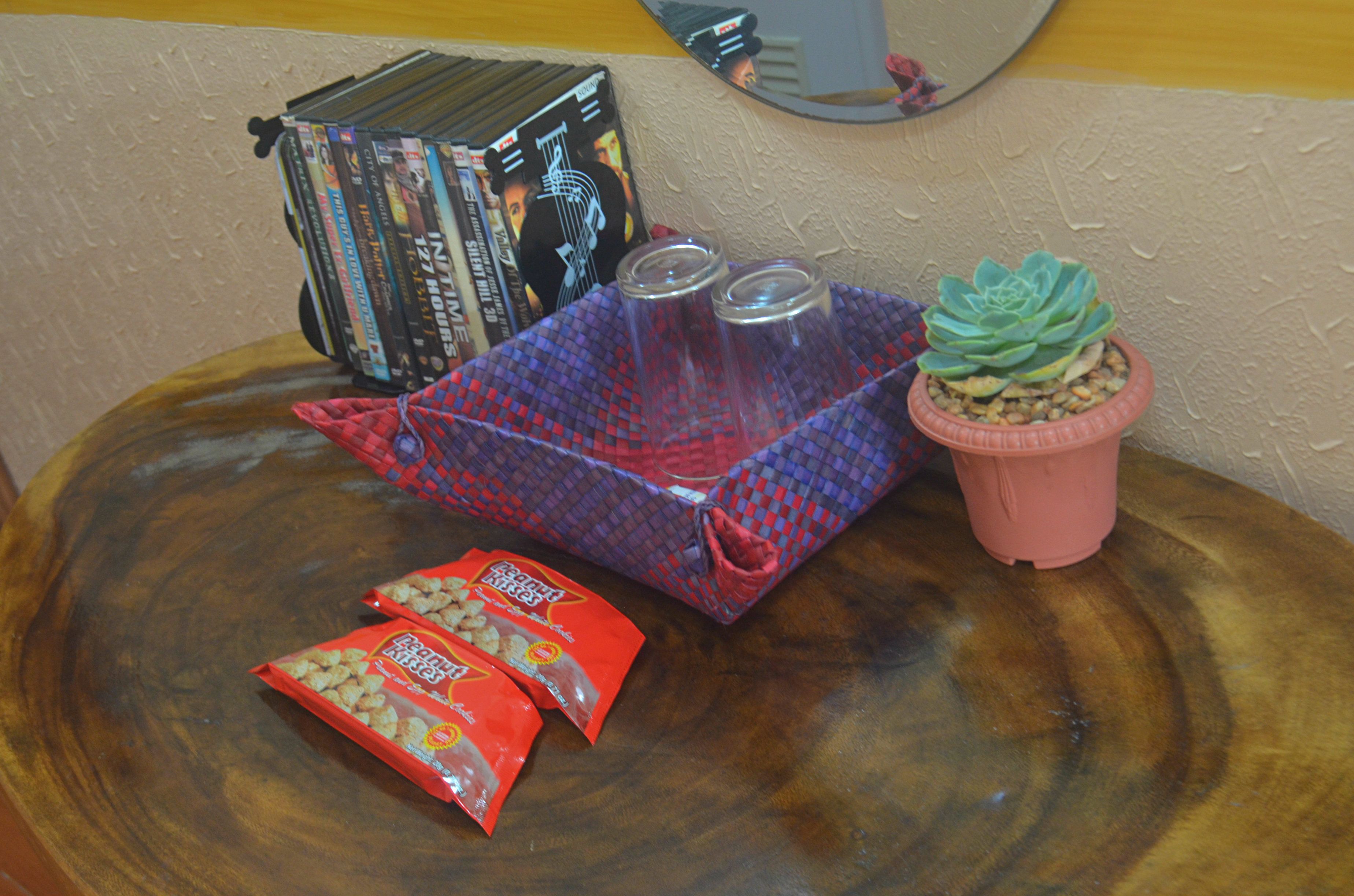 A wooden table with a DVD player, a small potted plant, two glasses, and two snack packets.