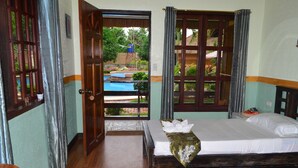 Une chambre d’hôtel avec un lit en bois, une vue sur une piscine et une porte donnant sur l’extérieur.