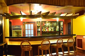 A bar area with a counter, wooden chairs, and a shelf with bottles. - Veraneante Resort (Panglao)