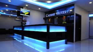 A reception desk with a blue-lit reception area, a flat-screen TV, and a sign for Cathay Hotel. - Cathay Hotel (Kota Kinabalu)