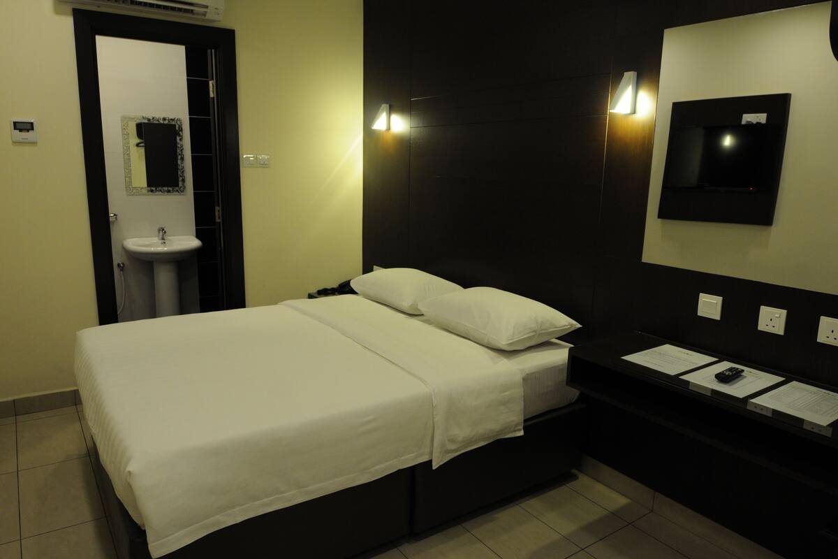 A hotel room with a bed, a bedside table, a mirror, a sink, and a wall-mounted TV.