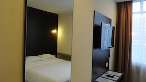 A hotel room with a bed, a flat-screen TV mounted on the wall, and a window with curtains. - Cathay Hotel (Kota Kinabalu)