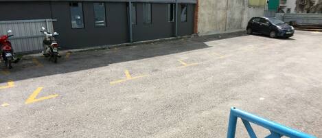 A parking area with a blue metal barrier, a red motorcycle, and a black car parked.