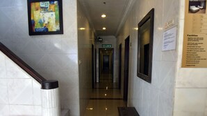 Un couloir d’hôtel avec un banc, un tableau encadré au mur et un panneau indiquant l’emplacement des téléphones portables.